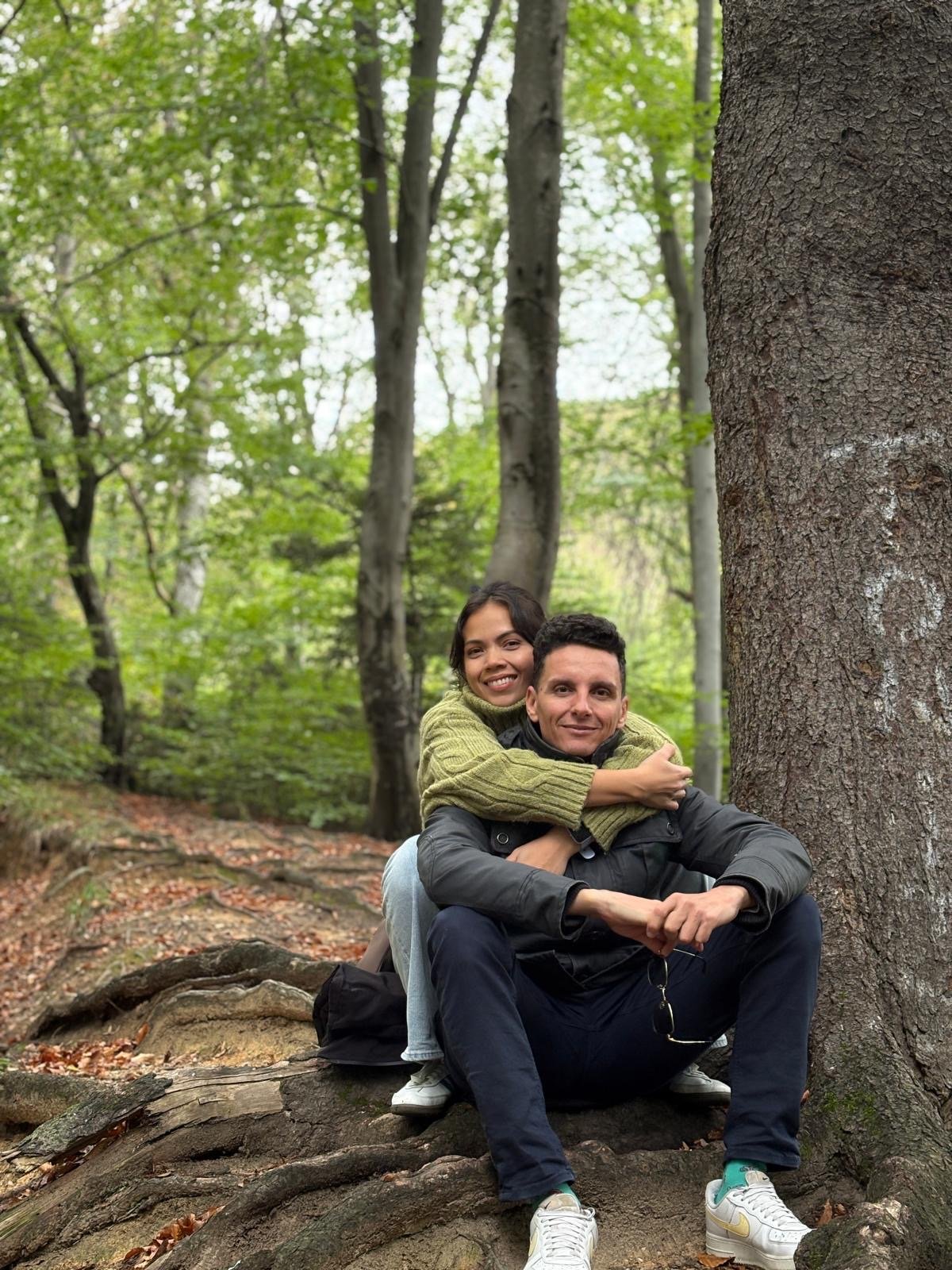 Trish and Suam sitting at the roots of a tree in the woods